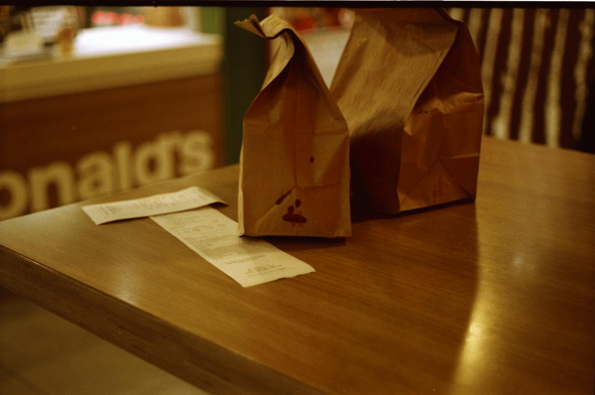 Retro-style brown paper bags and receipt at McDonald's table evoke a nostalgic fast food experience.