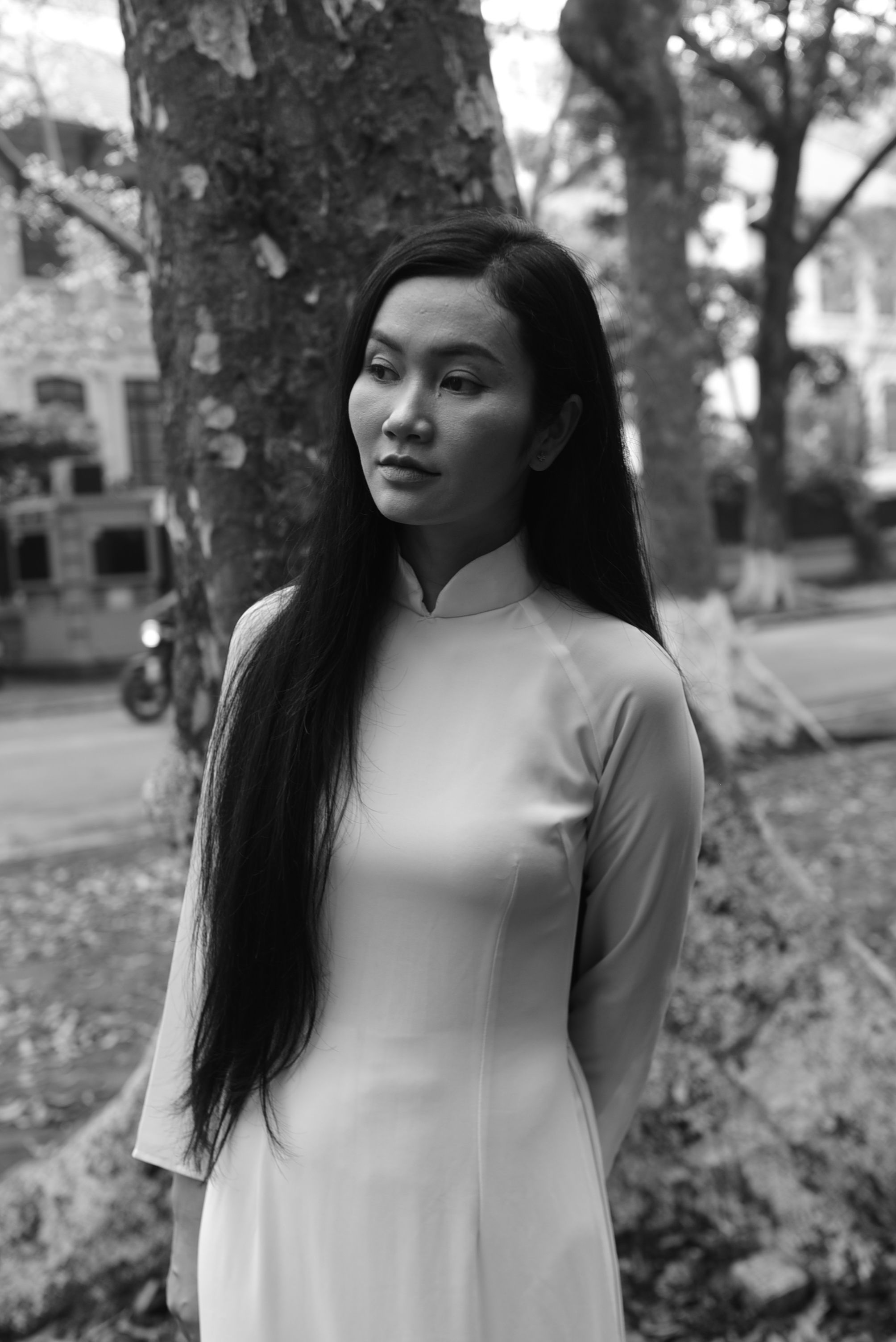 Black and white portrait of an Asian woman in an elegant dress standing in a park.