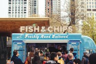 在一辆热闹的餐车前，人群正享用着炸鱼和薯条，背景是城市建筑