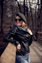 秋天，一位快乐的女子身着时尚皮夹克，头戴贝雷帽，在树林中摆出户外造型