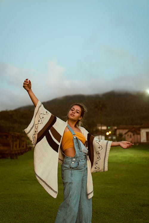 Photo of Woman Wearing Orange Crop Top and Dungaree Pants Posing With Her Hands Raised