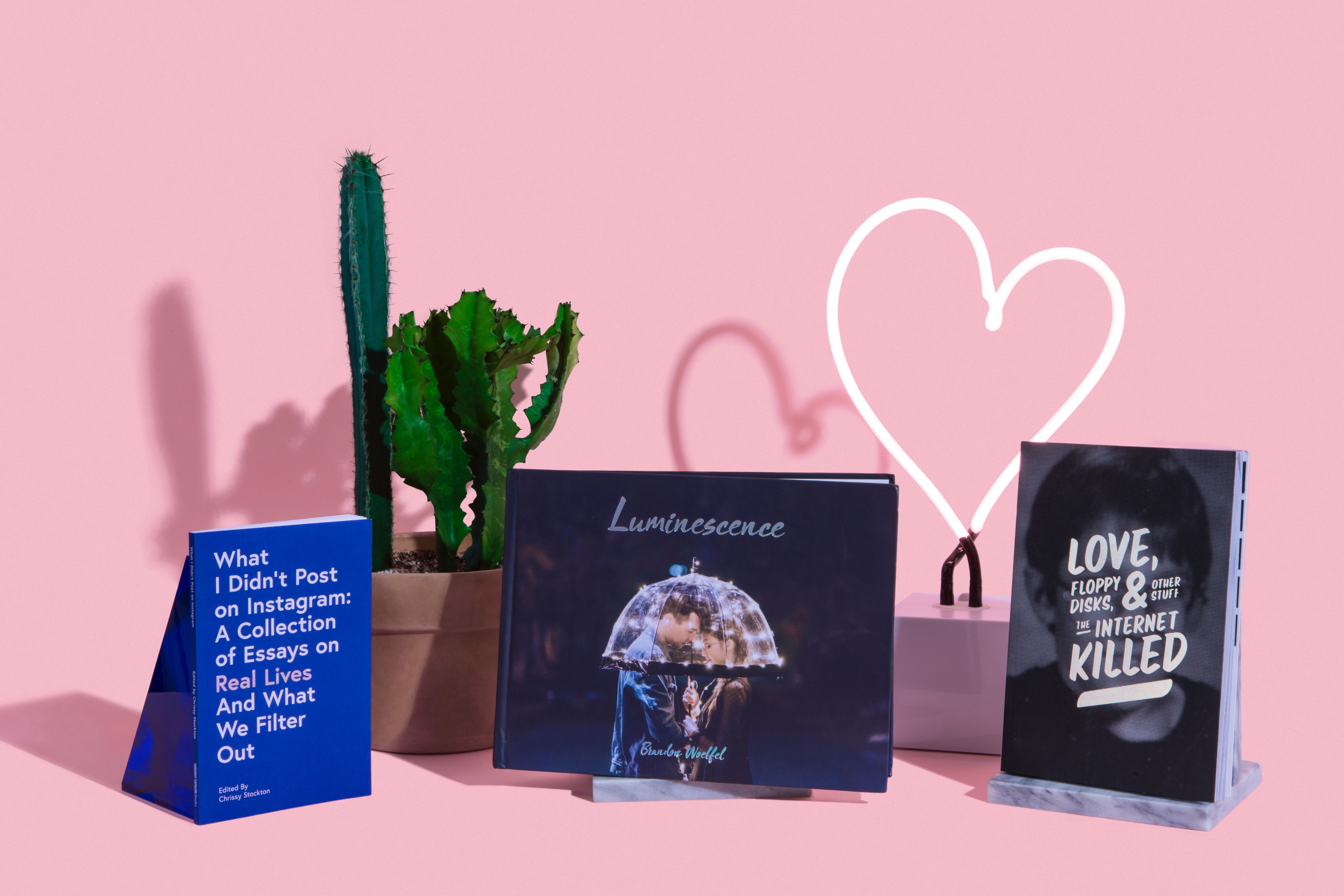 Books and a neon heart with a shadowed cactus on a pink background.