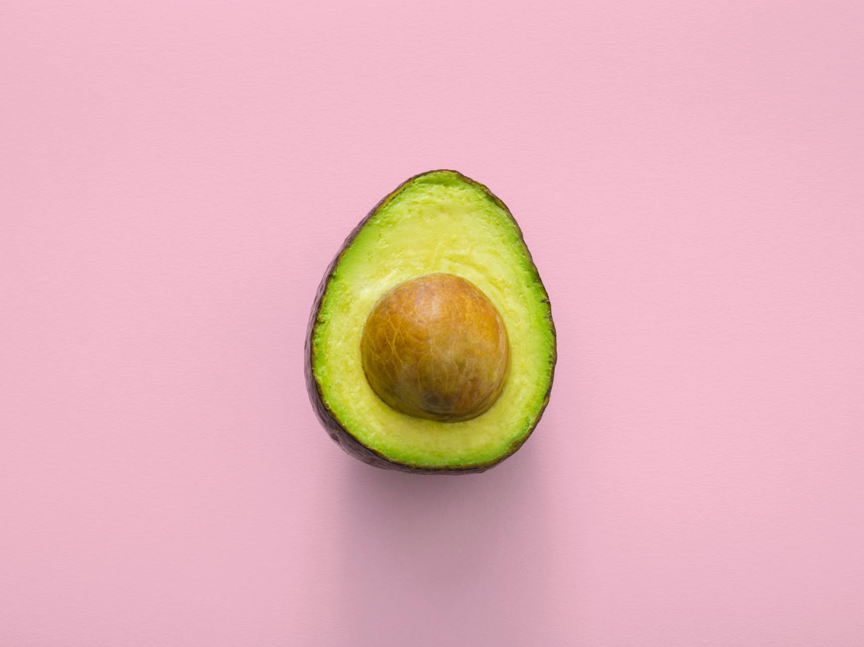 avocado cut in half kept on a pink background
