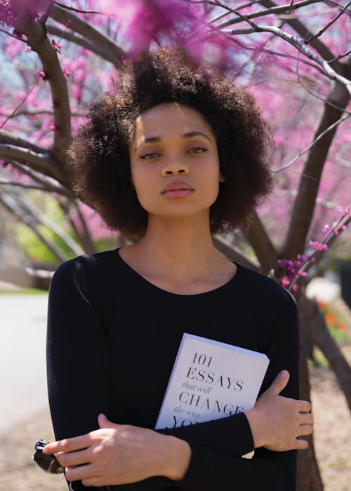 Free Woman Standing Beside Tree Holding Book Stock Photo