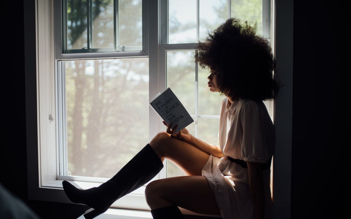 A woman enjoys a peaceful reading session by a window, bathed in natural light.