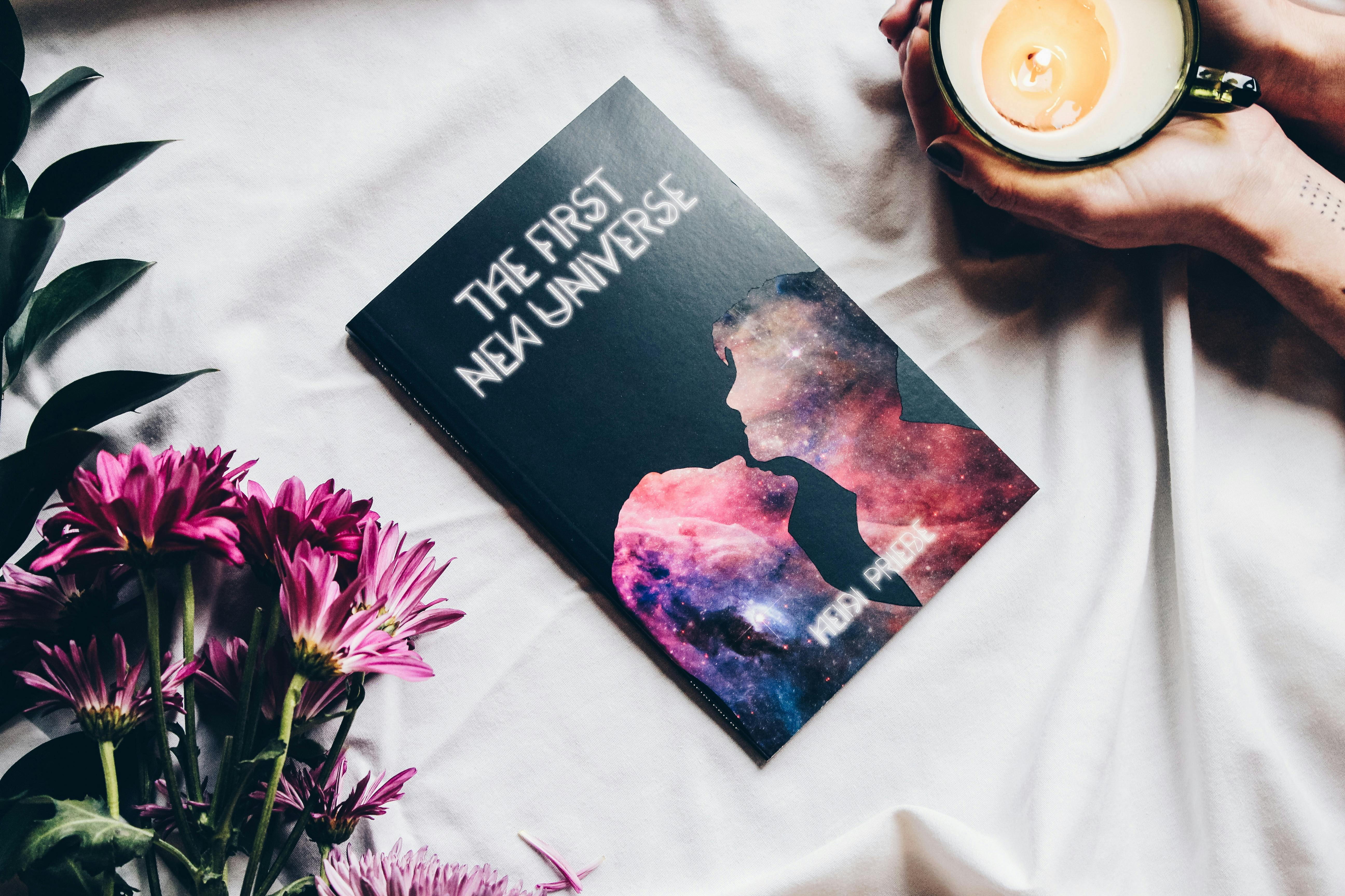 Artistic flat lay featuring a book, candle and flowers creating a cozy atmosphere.
