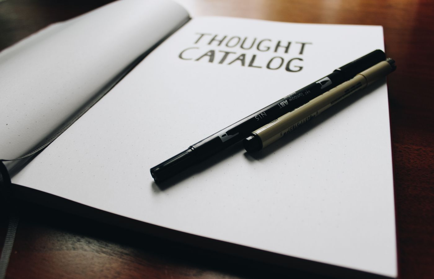 Open thought catalog notebook with pens on a wooden desk, ideal for writing inspiration.