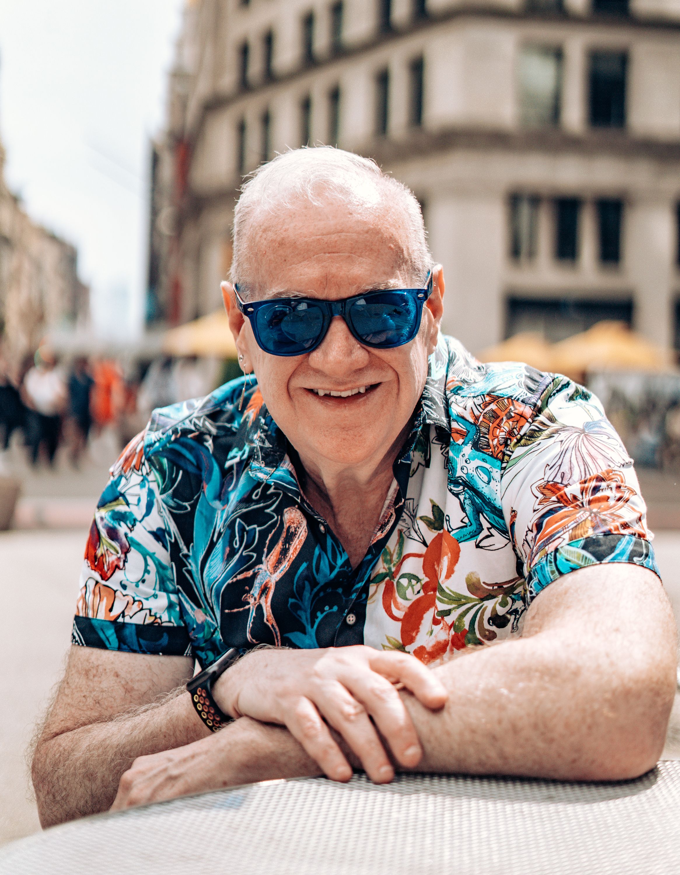 Smiling elderly man in vibrant shirt and sunglasses enjoying a sunny day outdoors.