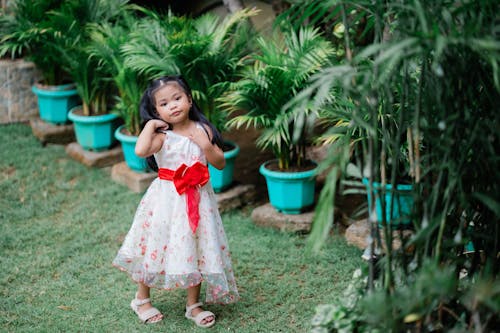 A little girl in a red and white dress standing in front of some plants