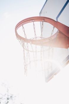 A close-up shot of a sunlit basketball hoop with metal chains, outdoors.