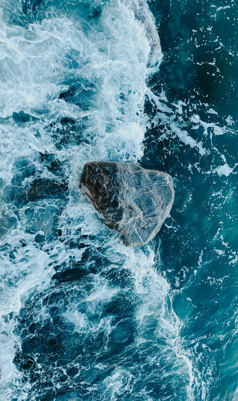 Dynamic aerial shot of ocean waves crashing into a solitary rock, showcasing nature's power.