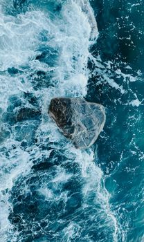 Dynamic aerial shot of ocean waves crashing into a solitary rock, showcasing nature's power.