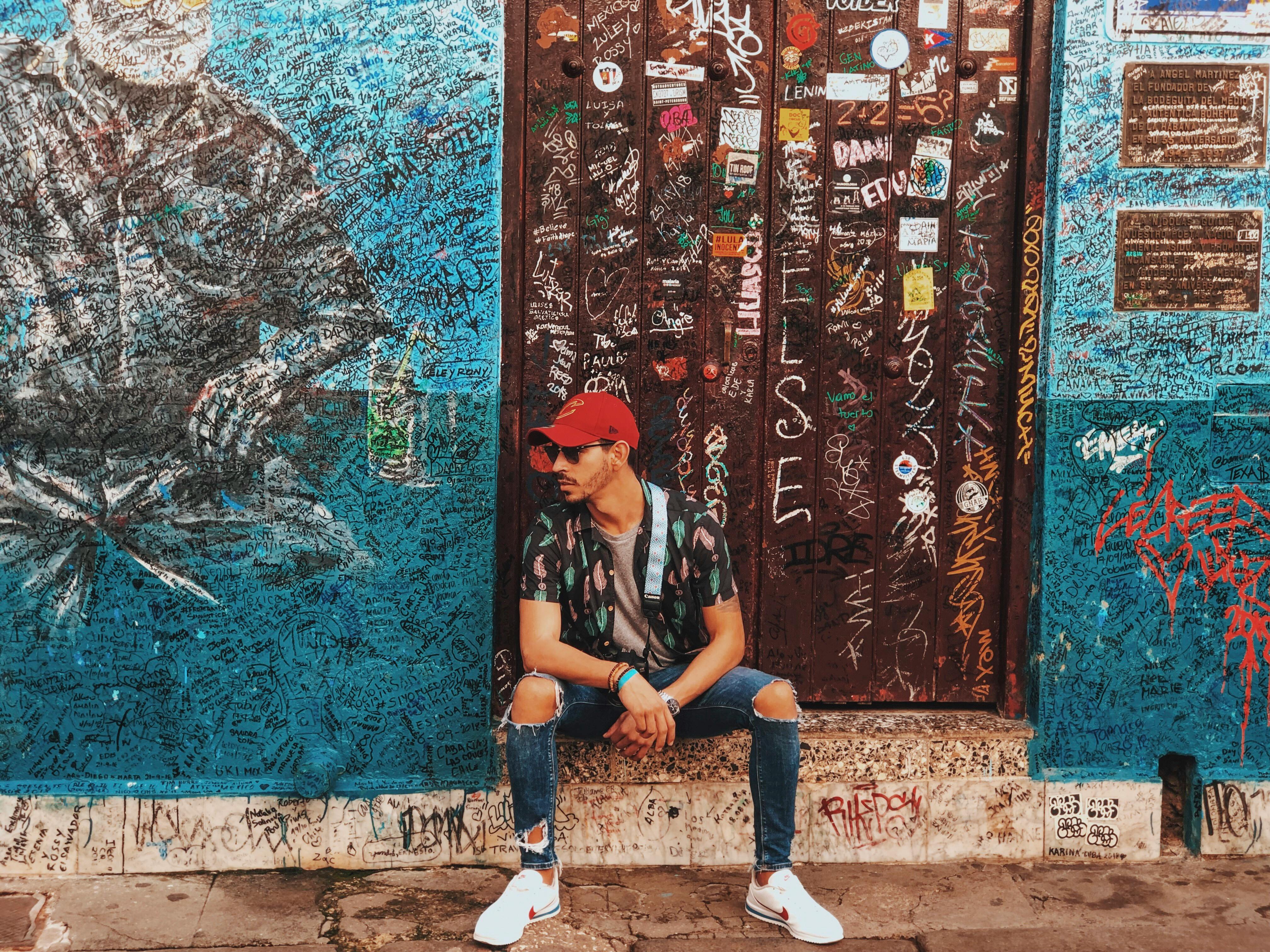 Stylish man in urban setting with graffiti wall and ripped jeans showcasing street fashion.