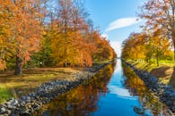 平静的运河中倒映着色彩缤纷的树木，构成一幅宁静的秋景