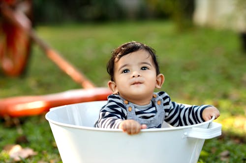 A baby in a white bucket sitting on grass