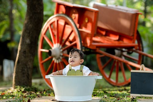 A baby in a bathtub with a wagon in the background