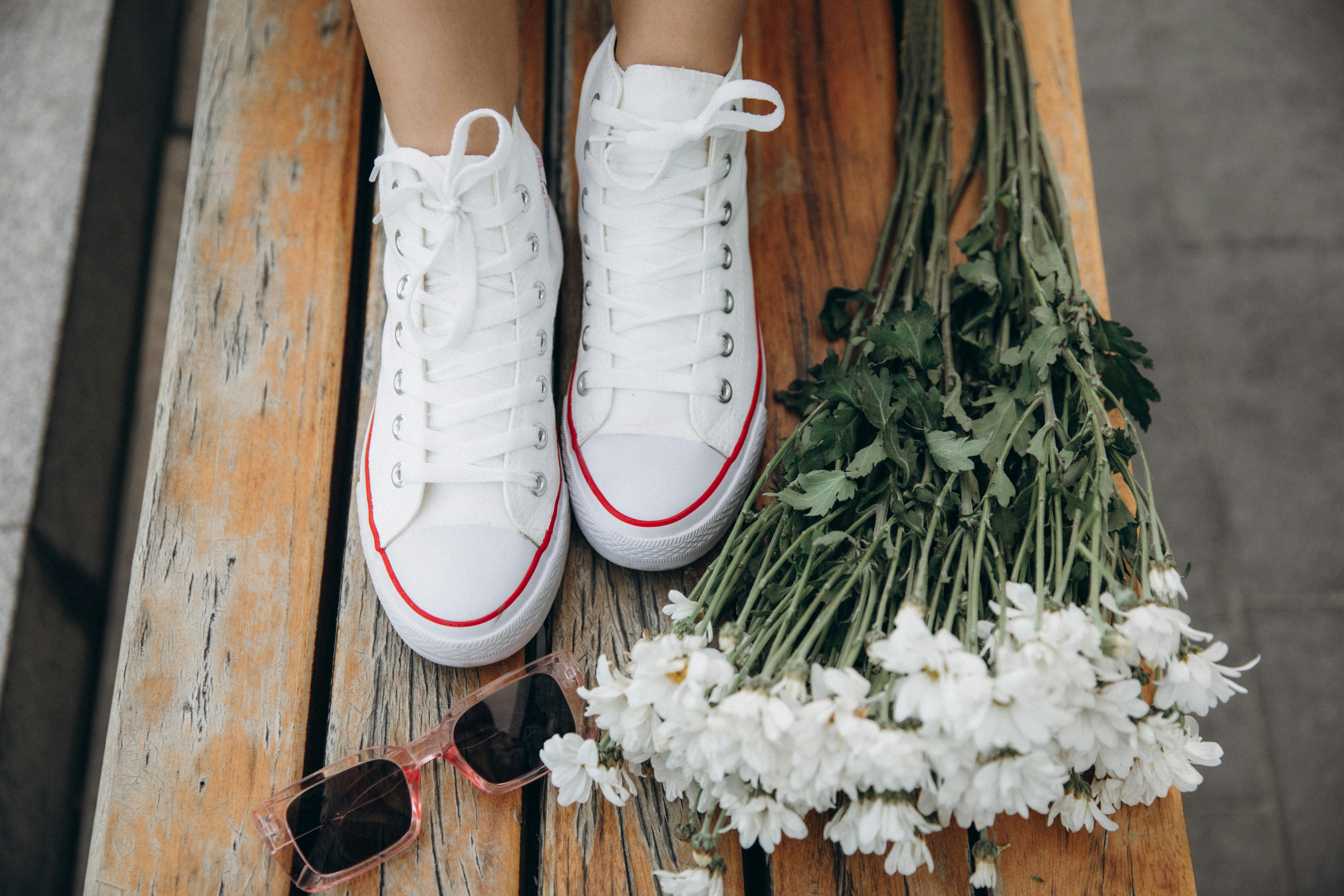 White high-top sneakers on wooden bench with sunglasses and daisies. Stylish and casual vibe.