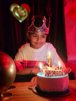 A young boy celebrates his birthday with a cake, crown, and candles, creating a joyful scene.