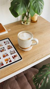 Warm home office setup featuring a cappuccino and tablet on a wooden desk.
