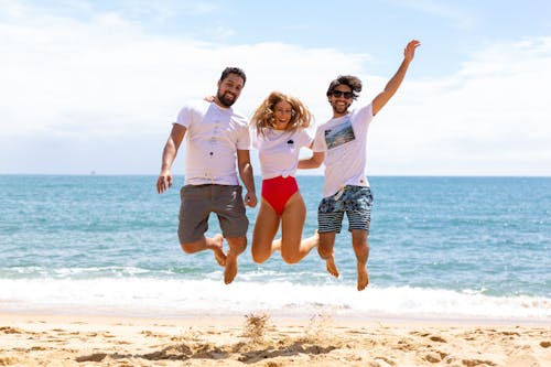 Free Two Men and One Woman Jumping Near Shore Stock Photo