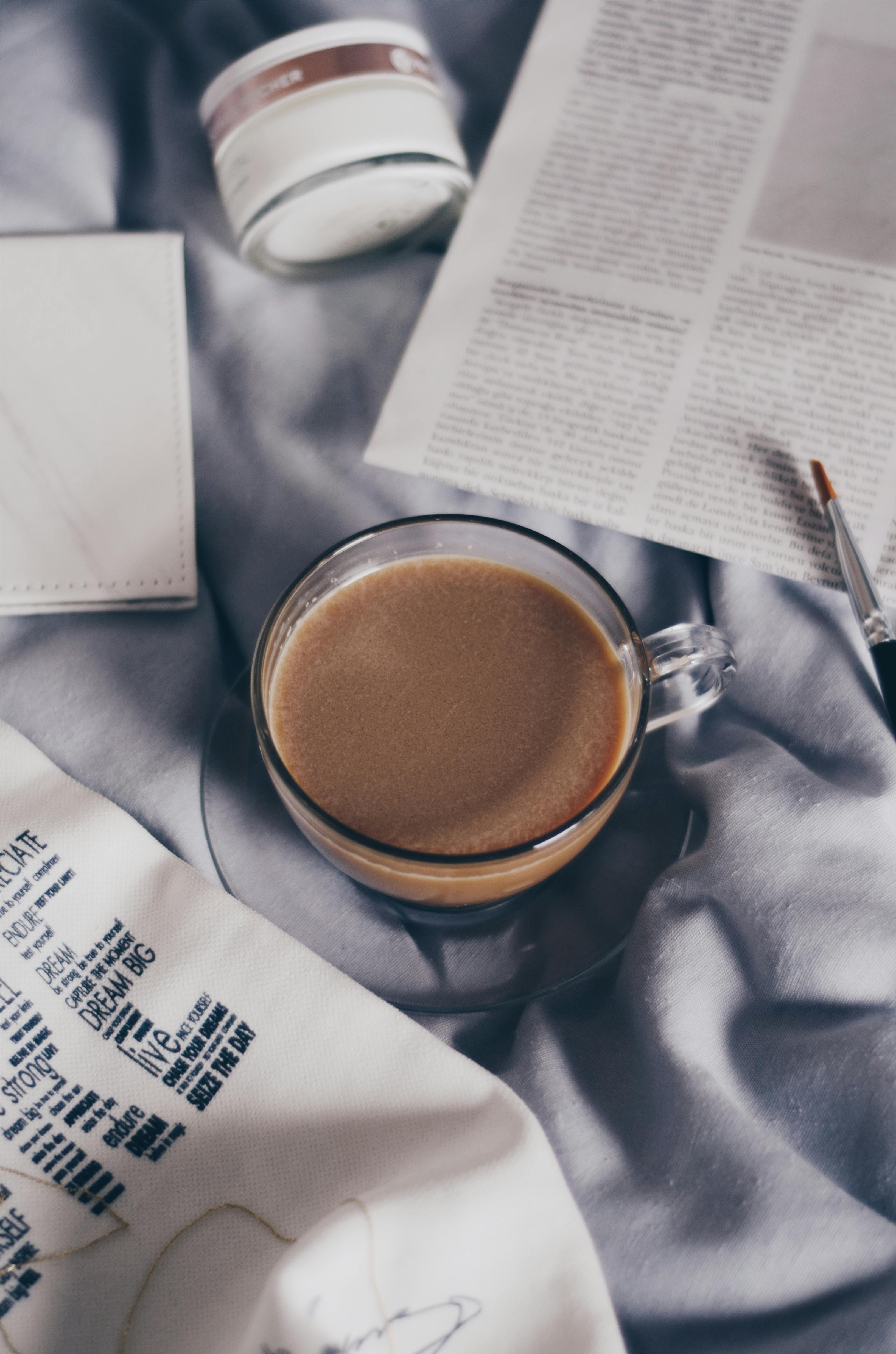 一杯热咖啡放在优雅的缎面床单上，旁边摊着报纸，营造出轻松的早晨氛围