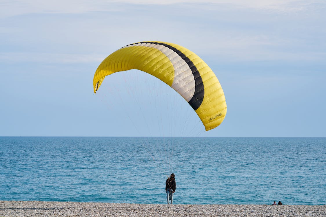 Free Person With Yellow and White Gliding Parachute Near Sea Stock Photo