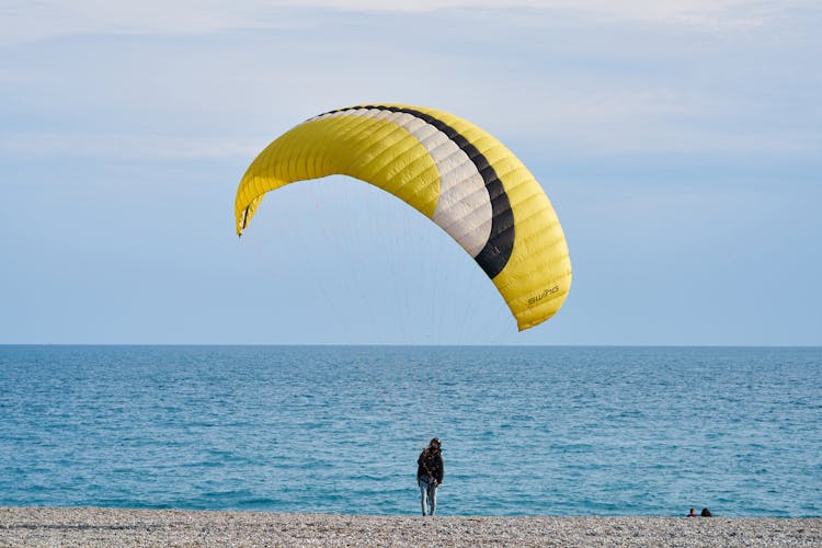 Person With Yellow And White Gliding Parachute Near Sea