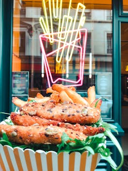 Close-up of crispy chicken strips with fries in a trendy neon-lit restaurant setting.