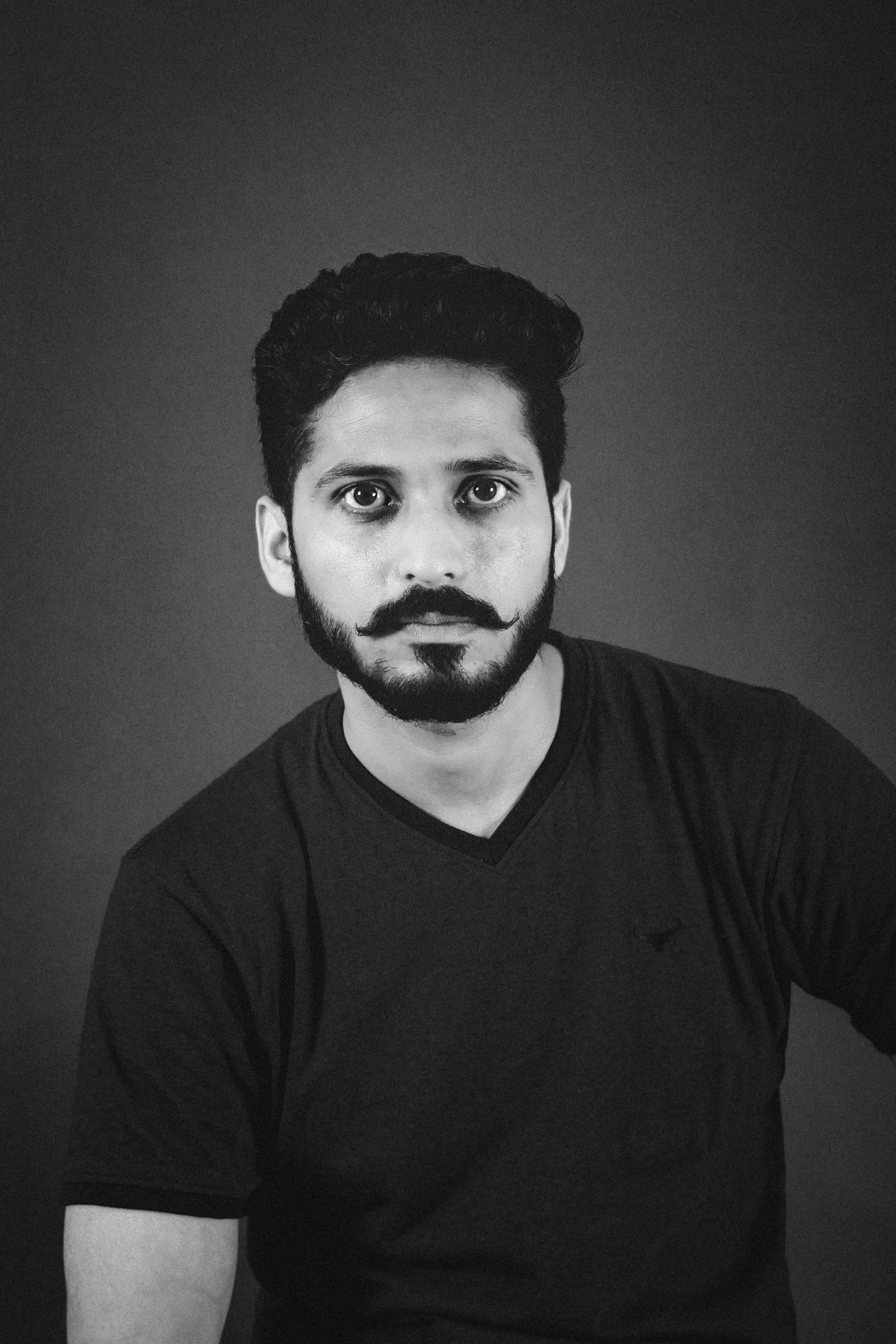 Monochrome portrait of a serious man with a distinct mustache, wearing a t-shirt.
