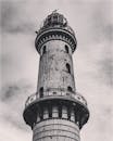 黑白照片从低角度拍摄了高耸的砖砌灯塔，映衬着戏剧性的多云天空