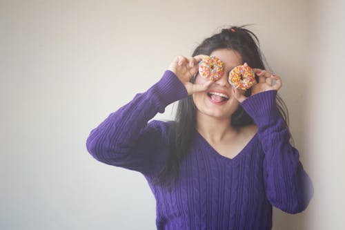 Женщина в свитере, закрывая глаза пончиками