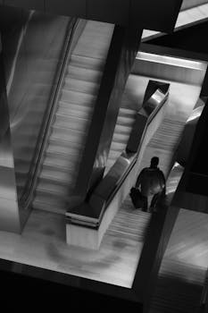 一张现代建筑内的单色图像，其中有一位男士，建筑内设有自动扶梯和楼梯