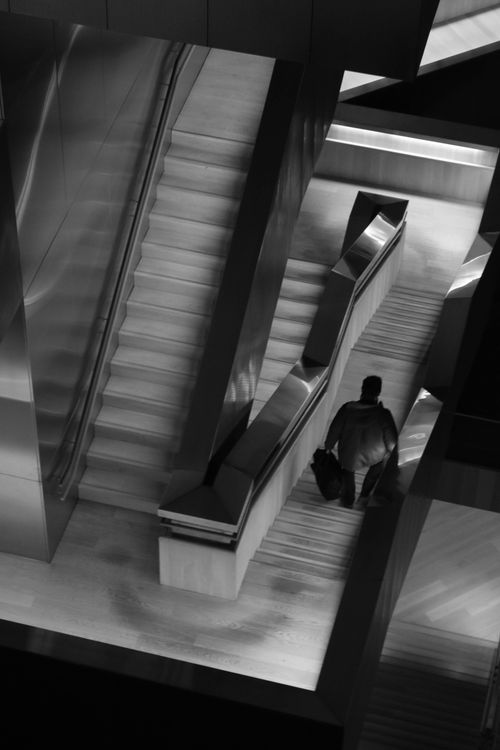 Free Monochrome image of a man in a modern building with escalators and stairs. Stock Photo