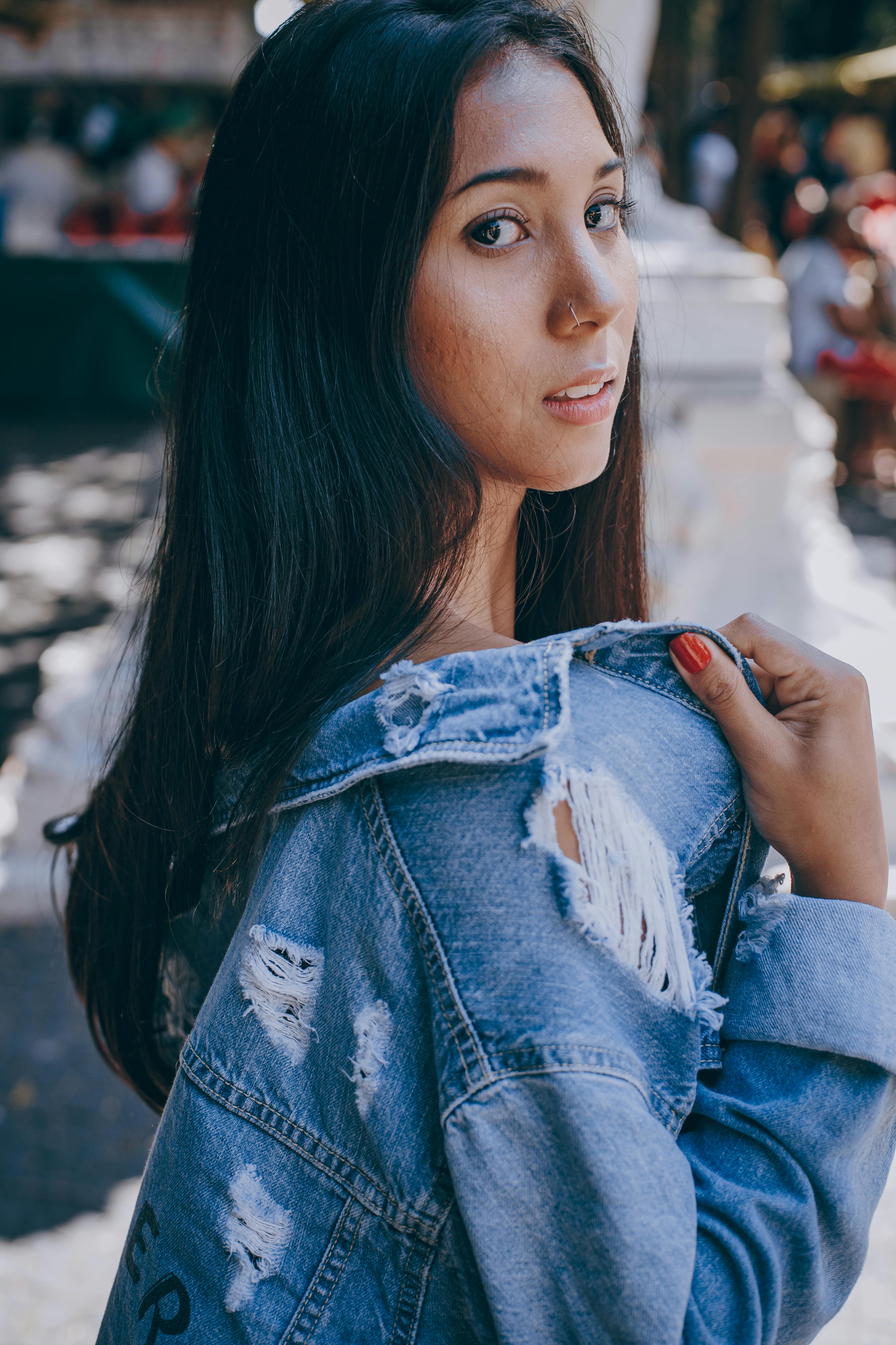 一位年轻女子穿着破旧牛仔夹克，在户外回头张望的肖像