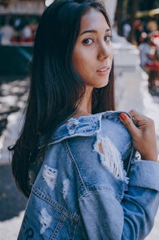 一位年轻女子穿着破旧牛仔夹克，在户外回头张望的肖像