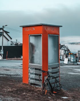 A classic red telephone booth stands in a quiet town, accompanied by a bicycle.