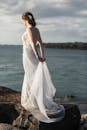 在岩石海岸上，一位新娘穿着飘逸的婚纱，俯瞰着大海