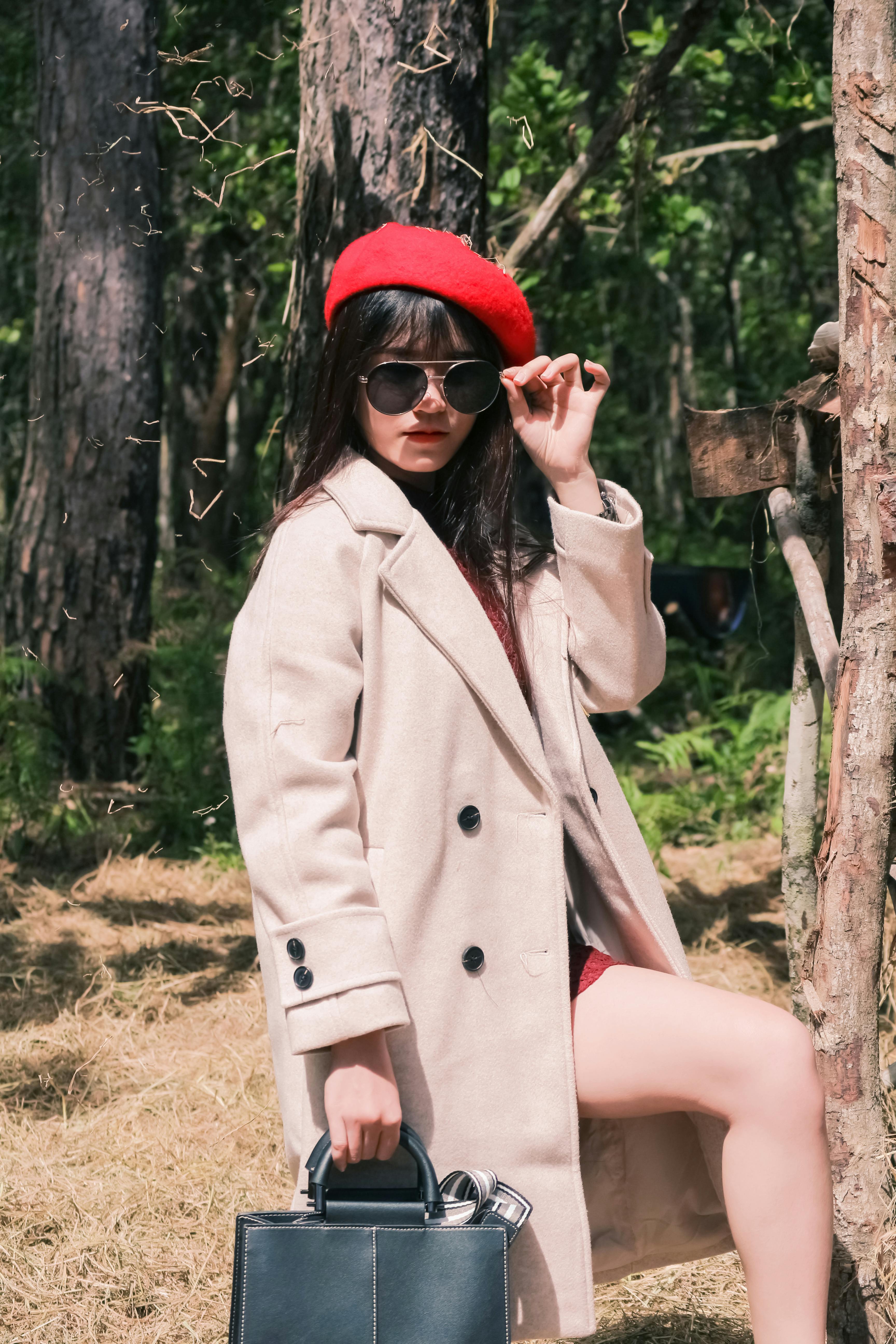一位穿着米色外套、戴着红色贝雷帽和太阳镜的时髦女人在森林里摆姿势
