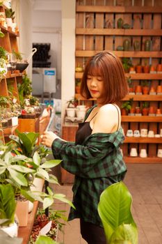 亚洲妇女在充满活力的植物与陶器环绕的室内花园中探索，画面以温暖的色调拍摄