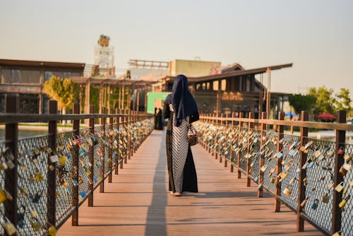 Person Walking on Wooden Pathway Beside Different Padlocks Hanging on Gray Stainless Steel Chain Link Fence