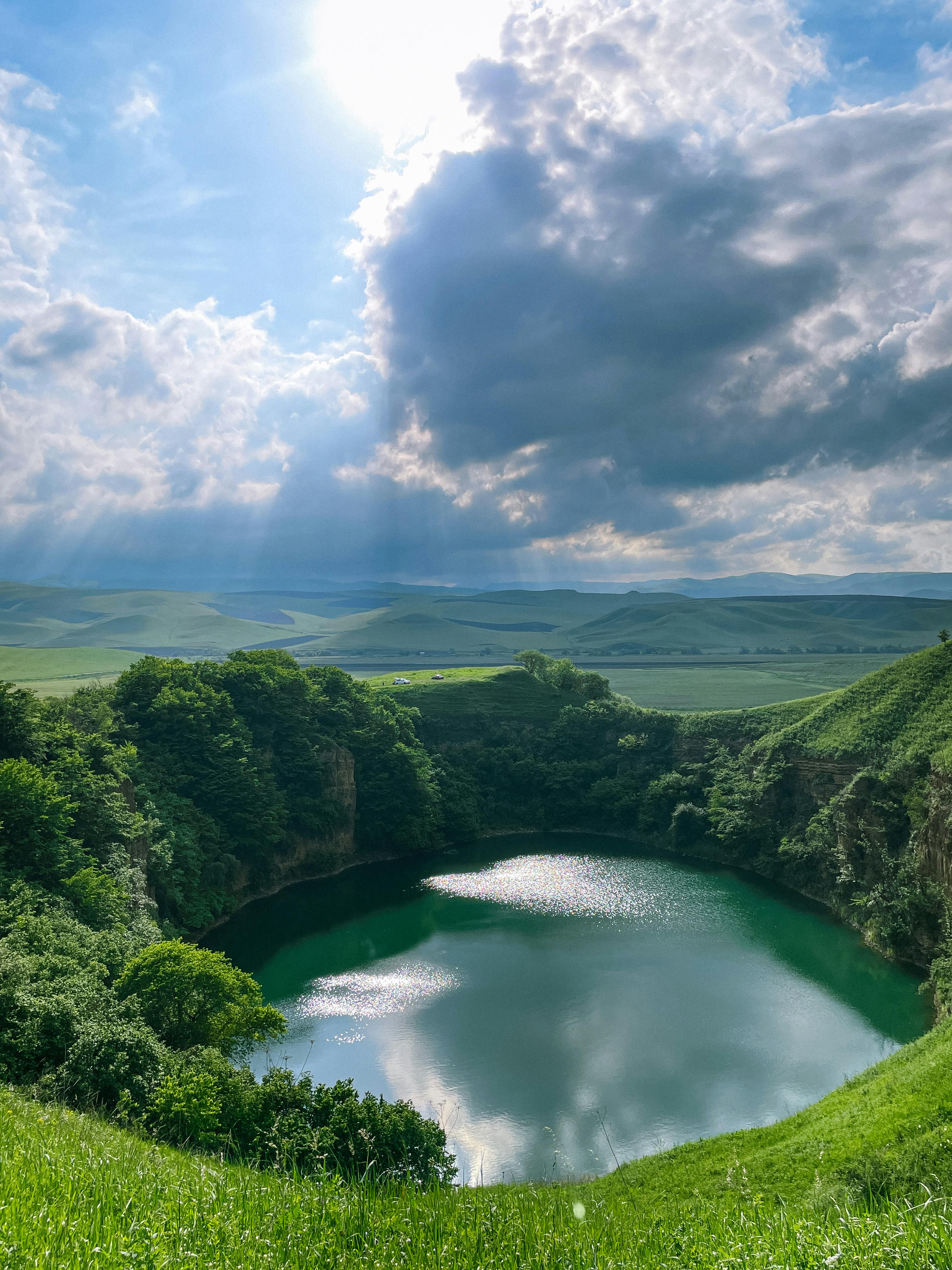 Beautiful landscape of Lake Shadkhurey surrounded by lush hills and dramatic skies.
