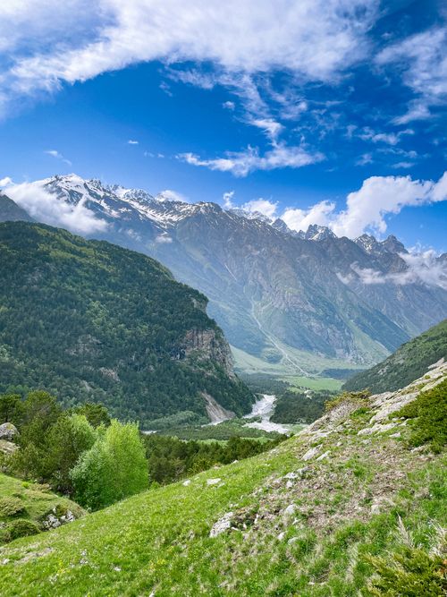 Free Breathtaking view of a lush green valley surrounded by majestic mountains and clear blue skies. Stock Photo