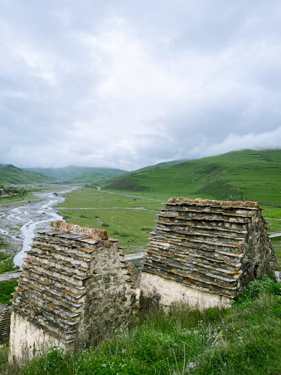 Two stone buildings sit on a hillside overlooking a river
