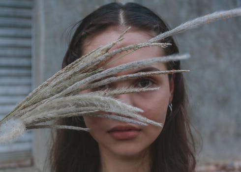 一幅女性艺术肖像中，草茎遮住了她的脸，营造出神秘而宁静的氛围