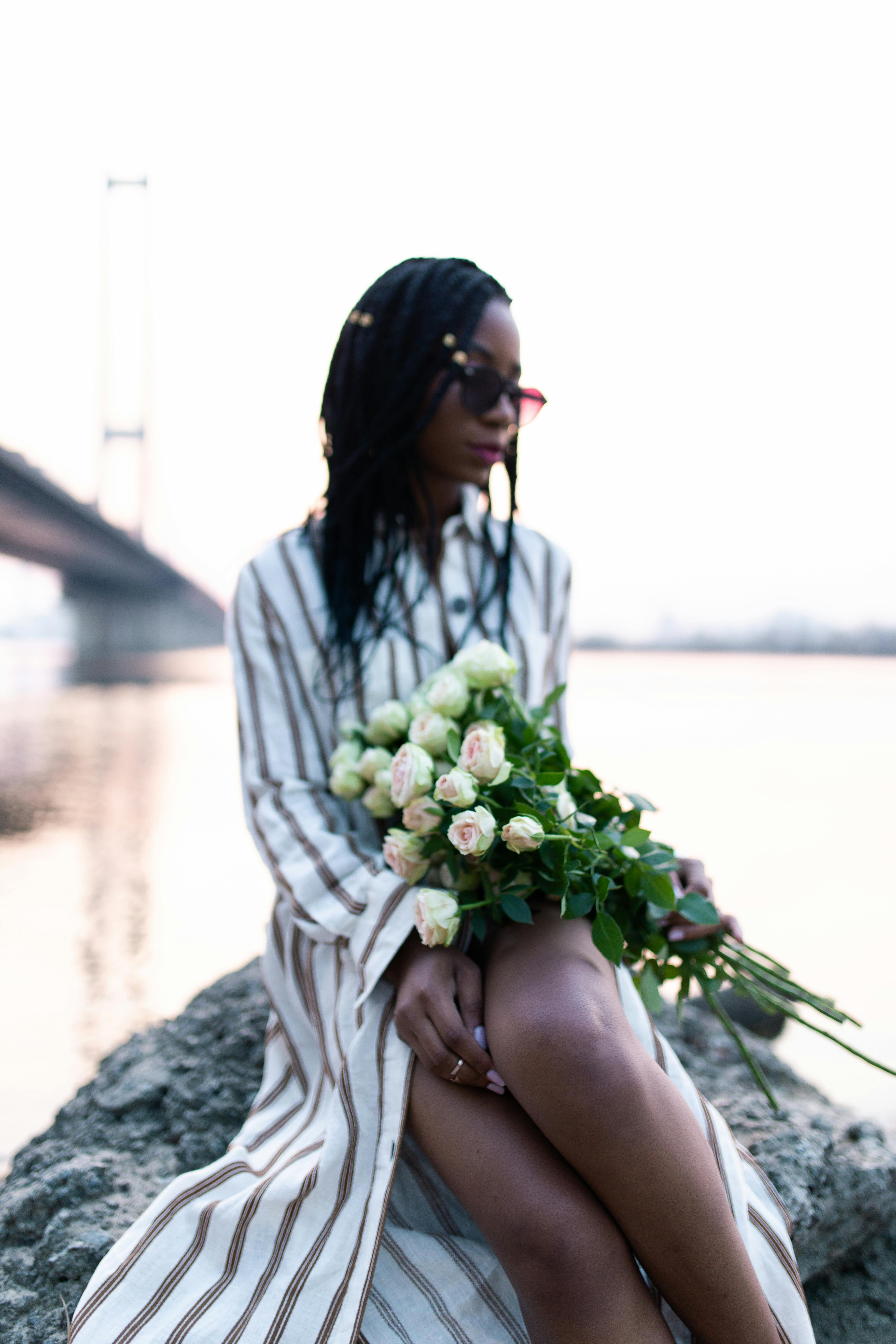 A contemplative woman holding white roses by the river at sunset.