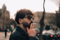A man with sunglasses and a beard is smoking a cigarette