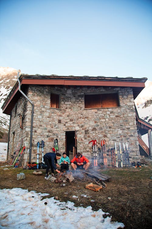 A group of people sitting around a fire in front of a stone building
