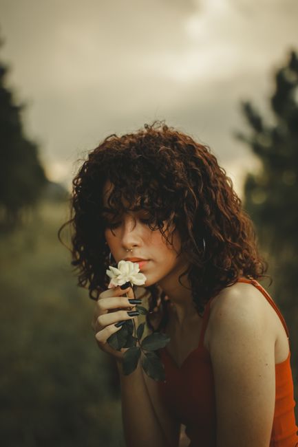 Artistic portrait of a woman holding a white flower outdoors, evoking a serene mood.
