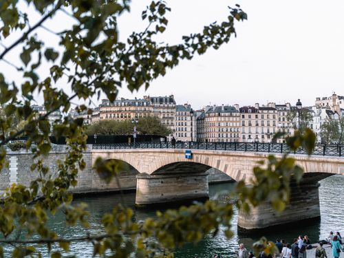 Free A scenic view of a Parisian bridge with historic buildings and trees. Stock Photo