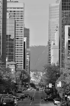 Black and white view of Vancouver street with skyscrapers and mountains in background.